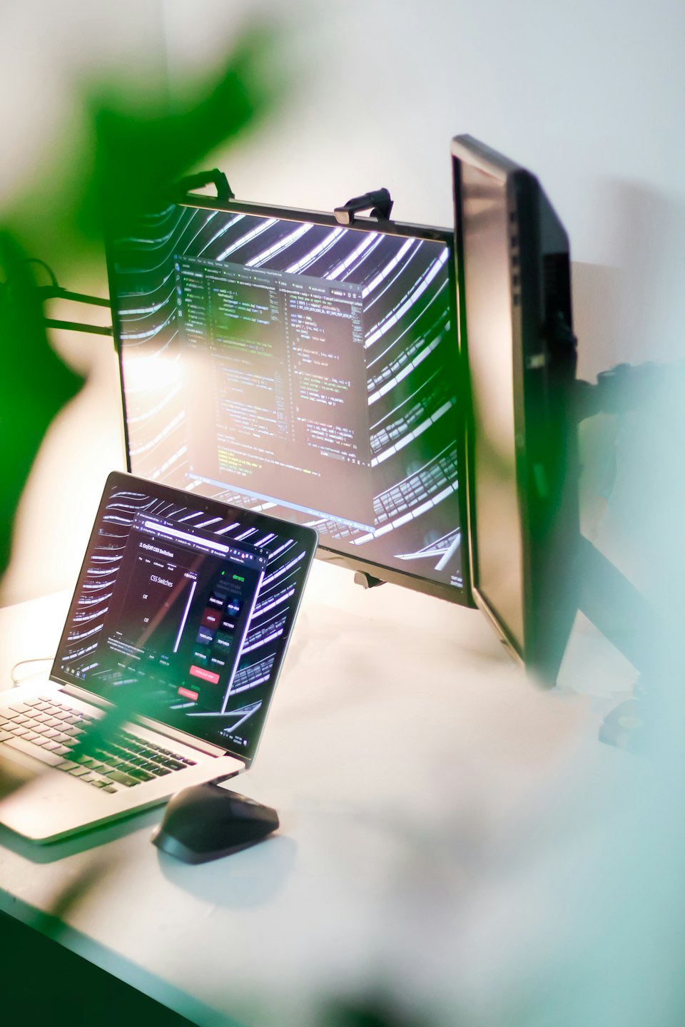 Laptop and dual monitors displaying code on a desk.